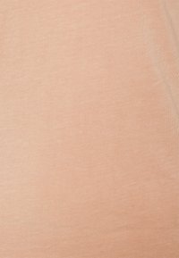 Světle broskvové tričko vyrobené z měkké, hladké látky. Má jednoduchou, ribbovanou texturu bez viditelných vzorů nebo akcentů.