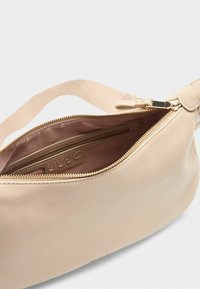Eine hellbeige Handtasche mit einem Reißverschluss, der ein glattes Innenleben offenbart. Das Markenlabel ist sichtbar und betont das stilvolle Design.