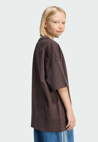 Tamno smeđa oversized majica kratkih rukava s okruglim izrezom i mekim materijalom; uparena s plavim širokim trapericama s bočnim trakama.