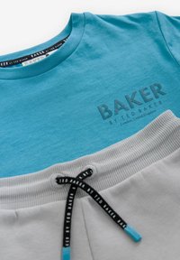 Heled sinine T-särk, millel on hall "BAKER" logo, koos hallide joggeritega, millel on soonikkoes vöökoht ja must pael logo detailidega.