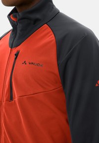 Rote und schwarze Zip-Jacke; verfügt über einen hohen Kragen, eine weiche Textur und eine seitliche Tasche mit Zuglasche. Logo auf der Brust angezeigt.