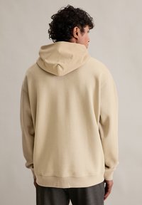 Beżowa bluza z kapturem, miękka w dotyku, luźny krój, ściągacze przy mankietach i dolnym brzegu. Bezszwowy design z tyłu, idealna do noszenia na co dzień.