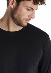 Camiseta negra de manga larga hecha de tela suave. Presenta un cuello redondo, un ajuste relajado y una textura lisa. Diseño minimalista, sin patrones.