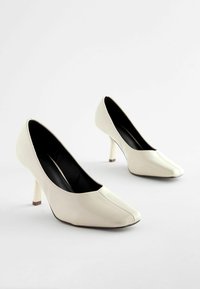 Talons hauts en cuir verni blanc avec un bout pointu et un design effilé. Les talons mesurent environ 7,5 cm de hauteur avec un intérieur noir.