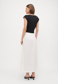Haut noir à manches courtes associé à une jupe blanche longueur cheville, présentant une texture lisse et une taille élastique. Sandales à talons noires complètent le look.