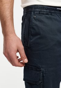 Cargo bukser i mørkeblå stof har en struktureret overflade, elastisk talje og flere sidelommer med knap- og lynlåsdetailler.