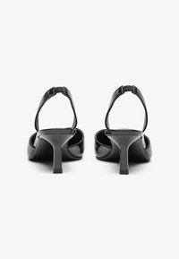 Μαύρα παπούτσια με λουράκι στη φτέρνα από παρμπρίζ δέρμα, με καμπυλωτή τακούνι, ελαστικό λουράκι πίσω και ανοιχτή μύτη. Λείο επιφάνεια με γυαλιστερό φινίρισμα.