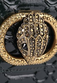 Chiusura in oro e nero a forma di testa di pantera stilizzata su pelle nera lucida con texture coccodrillo.