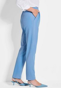 Hellblaue maßgeschneiderte Hosen mit Seitentaschen, geradem Bein, weichem Material und einem Saum, der knapp über dem Knöchel endet, kombiniert mit passenden spitzen Schuhen.