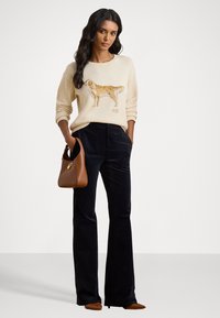 Beige knitted sweater with a dog design, paired with dark blue corduroy pants. Brown handbag with a gold clasp and heeled shoes.