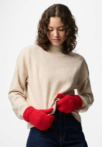 Maglione beige in maglia con collo alto, abbinato a guanti rossi in maglia. Il maglione presenta una vestibilità comoda; i guanti hanno polsini a coste e un tessuto strutturato.