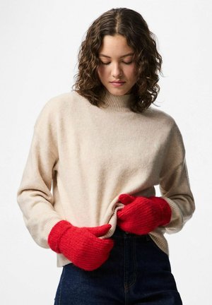 Beige gebreide trui met een hoge nek, gecombineerd met rode gebreide handschoenen. De trui heeft een ontspannen pasvorm; de handschoenen hebben geribbelde boorden en een textuurstof.