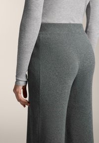 Sivý rebrovaný sveter a tmavošedé pletené nohavice s priliehavým pásom, ktoré zobrazujú jemnú textúru a hladký materiál v ležérnom strihu.