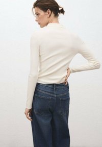 Haut à manches longues côtelé couleur crème associé à un jean en denim bleu foncé taille haute. La tenue présente un col et des poches arrière.