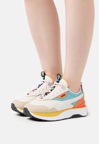 Baskets légères avec une tige beige et aqua, des accents orange et jaune, des matériaux texturés et des détails complexes de lacets.