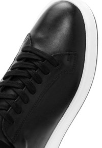 Basket noire en cuir avec des lacets plats noirs, bout arrondi, semelle en caoutchouc blanche et détails de couture subtils le long de l'empeigne.
