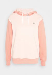 Ljust rosa och persika Nike-hoodie med framficka, vita dragsko och liten silverfärgad Nike-logotyp på vänster bröst.