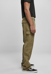Pantalons cargo en coton vert olive avec poches latérales, coupe décontractée, jambes droites, associés à des baskets noires avec des accents blancs.