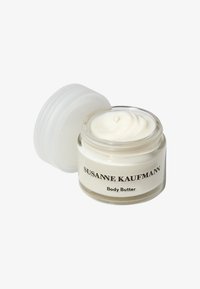 Pot en verre de beurre corporel avec une texture crémeuse blanche. Le couvercle est transparent, et le pot arbore un texte noir indiquant "Susanne Kaufmann Body Butter."