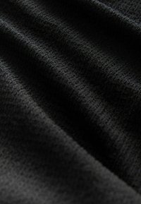 Schwarzer strukturierten Stoff mit feinem, gemusterten Gewebe, der weiche Falten zeigt und eine gleichmäßige matte Oberfläche hat. Das Licht spiegelt sich dezent von der Textur wider.