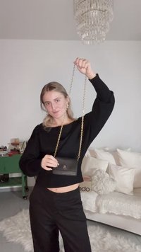 Black leather crossbody bag with a gold chain strap, featuring a small logo on the front. Smooth texture and compact rectangular shape.
