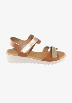 Sandalia marrón con tiras ajustables metálicas doradas y suela blanca texturizada, con diseño de punta abierta y cuña baja.