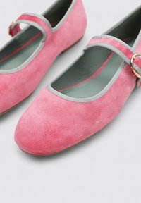 Bailarinas de ante rosa con punta redondeada, ribete gris y una correa delgada con un hebilla tono dorado. Forro interior suave.