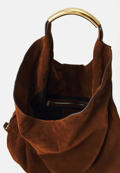 Sac fourre-tout en suède marron avec une poignée circulaire dorée, doté d'une poche zippée intérieure et d'une finition douce et texturée.