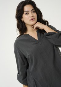 Blouse noire à col en V, dotée de manches trois-quarts, d'une texture douce et de rayures verticales subtiles, offrant une coupe décontractée.