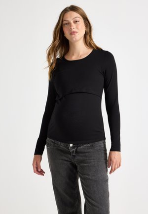 Svart långärmad topp med en rundad halsringning och en lagerdesign. Tillverkad av ett mjukt, elastiskt tyg. Matchad med mörkgrå jeans.