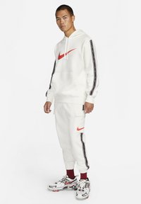 White hoodie and sweatpants with red Nike logo, black and red side stripes, and textured fabric; paired with athletic sneakers.