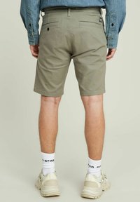 Pantaloni corti khaki realizzati in cotone leggero, con vestibilità dritta, due tasche posteriori e orlo arrotolato, abbinati a calzini bianchi e sneaker.
