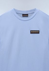 Lys blå bomulds t-shirt med rund halsudskæring og korte ærmer. Har et rektangulært sort stofmærke med brandlogo på brystet.