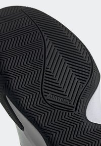 Semelle de chaussure en caoutchouc noir avec motif de bande de roulement en zigzag détaillé et marquage "ADIWEAR" près du centre.