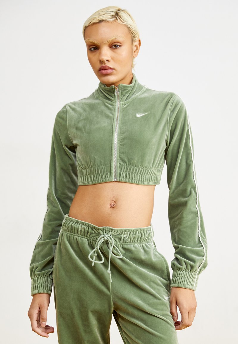 Conjunto de chándal de terciopelo verde que incluye una chaqueta corta con cremallera y cuello alto, y pantalones a juego con cintura elástica y cordones.