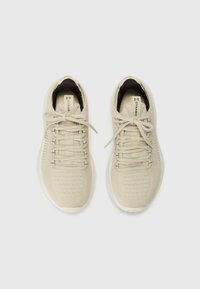 Lys beige sportsko med en tekstureret strikoverdel, flade snørebånd og en hvid gummisål. Enkel design med minimal dekoration.