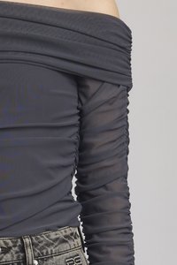 Avkortet topp i mørkegrått stoff med rynkete tekstur; gjennomsiktige lange ermer og tettsittende liv kontrasterer med mønstrede denim-bukser.