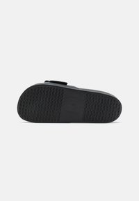 Schwarzes Schuhwerk mit einer strukturierten Gummisohle, einem weichen Obermaterial und minimalistischen Design, akzentuiert durch einen einstellbaren Riemen.