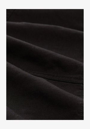 Must mustrakk, millel on sile tekstuur ja kerge sära. Omab peeneid õmblusi ja õrnu kortse, mis viitavad paindlikule materjalile.