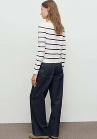 Gestreepte longsleeve shirt in wit en marineblauw, gecombineerd met wijde spijkerbroek in donker denim. De outfit heeft een relaxte fit en een minimalistisch ontwerp.