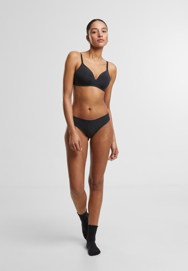 Zwarte lingerie set met een gladde, gevoerde beha met verstelbare bandjes en bijpassende low-rise slipjes, gepresenteerd op een model.