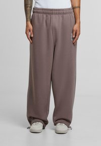Baggy sweatpants in muted brown cotton blend, featuring an elastic waistband, side pockets, and subtle logo accent on the thigh.