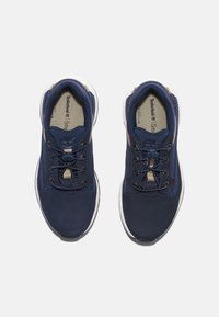 Marinblå textila sportskor med beige detaljer, rund tå och vit gummisula. Har snörning och texturerade stoffdetaljer.