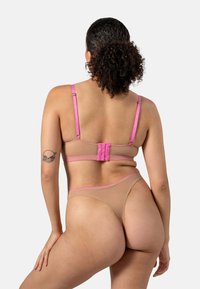 Beige lingerieset met roze accenten; bevat een aansluitende bh met verstelbare banden en haaksluiting, gecombineerd met een string. Zachte textuur.
