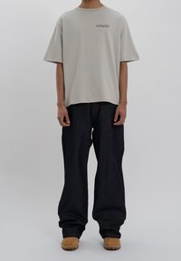 Camiseta de manga corta gris claro con logo bordado, combinada con unos vaqueros de mezclilla oscuros de corte suelto y botas de tobillo en color canela.