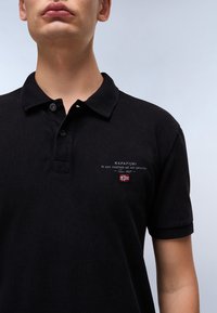 Svart polo skjorte laget av teksturert bomull med krage, to knapper og brodert logo på venstre bryst som har det norske flagget.
