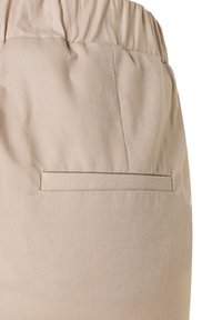 Beige pants with an elastic waistband and a horizontal slit back pocket without closure details, showing fabric texture and stitching.