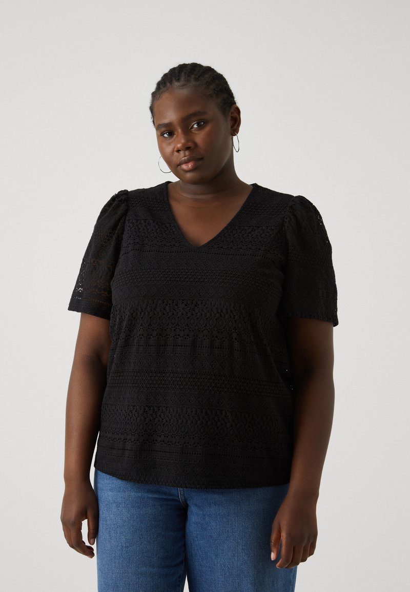 Black patterned top with a V-neck and short puff sleeves, featuring textured knit details. Paired with blue jeans.