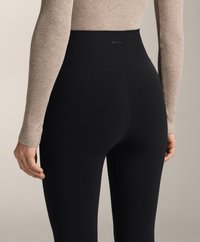 Črne visokotahle legice iz raztegljivega materiala, ki imajo gladek pas z diskretno blagovno znamko in oblikovan dizajn za eleganten videz.