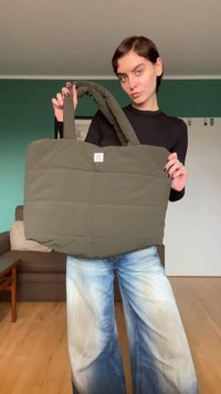 Gepolsterte Einkaufstasche in olivgrün mit doppelten Griffen, rechteckiger Form und einem Logopatch auf der Vorderseite. Strukturierter Stoff mit abgesteppten Abschnitten.